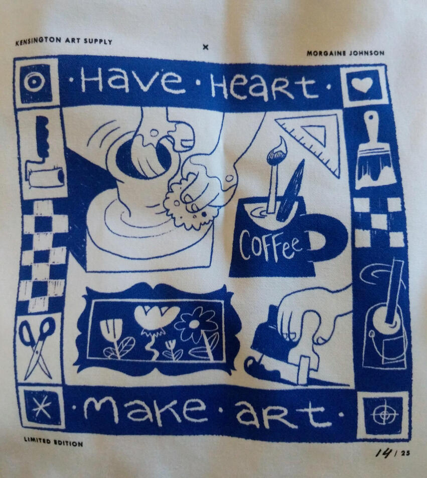 a tote bag printed depicting the words "have heart, make art", there are hands pulling a squeegee and throwing pottery, a coffee mug with paint brushes in it and framed artwork